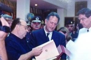 Ο πρόεδρος του Αναγνωστηρίου Αγιάσου Κλεάνθης Κορομηλάς προσφέρει στον υπουργό Εσωτερικών, Δημόσιας Διοίκησης και Αποκέντρωσης, Κώστα Σκανδαλίδη, τις εκδόσεις του ιδρύματος κατά την εκεί επίσκεψή του (16-8-2001). Δεξιά ο Νίκος Σηφουνάκης. 