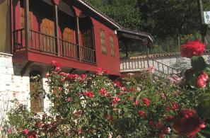 Το σαχνουσίνι της πρόσοψης του Λαογραφικού Μουσείου Αγιάσου πάνω από τις ανθισμένες τριανταφυλλιές του κήπου.